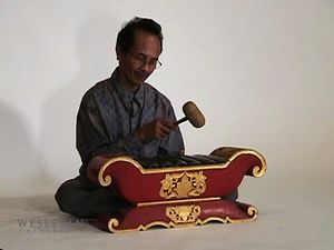 Observe a man playing the saron barung, a musical instrument of Javanese gamelan music