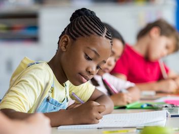 Girl student writing in her notebook in classroom in school.